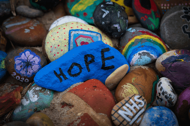 A pile of painted rocks, the top one of which has the word HOPE written on it.